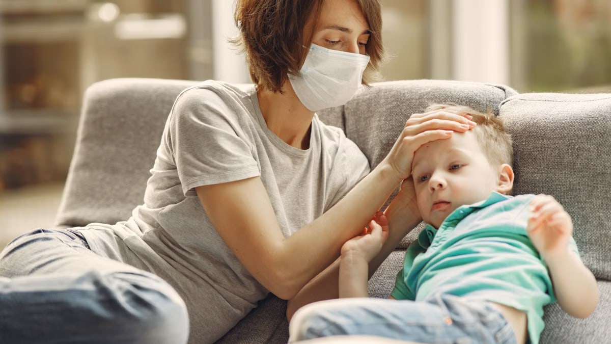 Caring mother wearing a mask comforts her sick son on the sofa, showing love and protection.